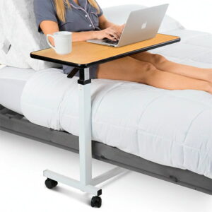 Vive Overbed Table with wood-grain top rolled over a bed, laptop on the table