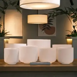 Seven white TOPFUND crystal singing bowls in graduated sizes arranged on a wooden shelf with a TOPFUND striker