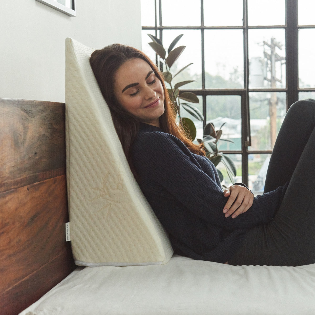Sloped foam wedge pillow with removable stretch-knit cover resting on a bed — view 2