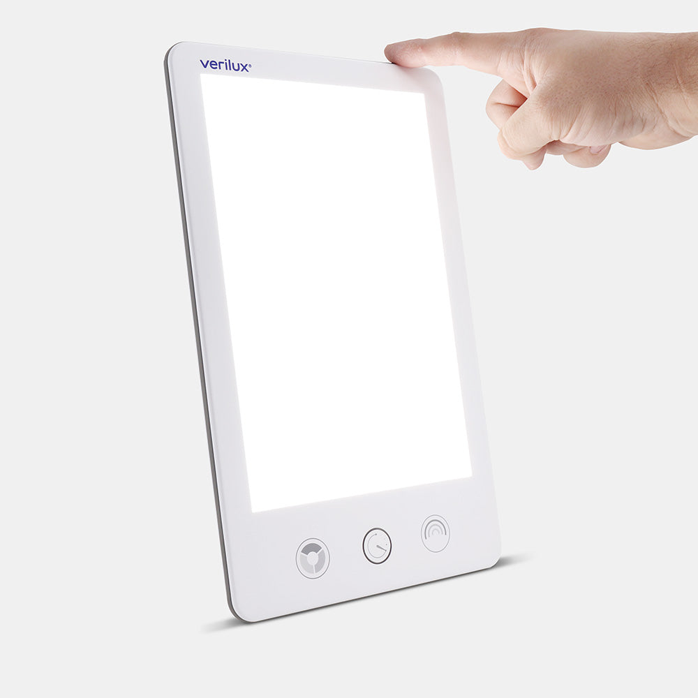 Verilux HappyLight Luxe, white, front view, with a finger on the top-edge power button
