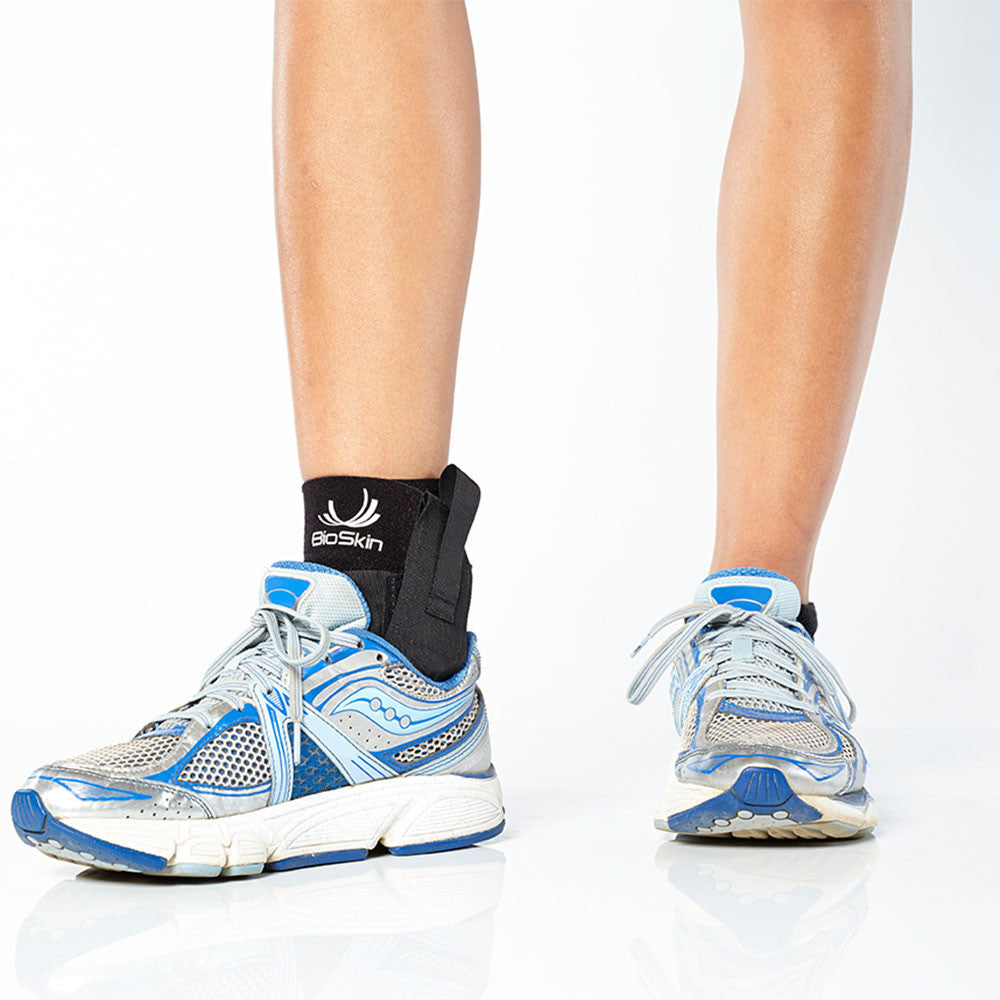 BioSkin black pull-on ankle support sleeve with stabilizing straps wrapped around a foot and ankle — view 2