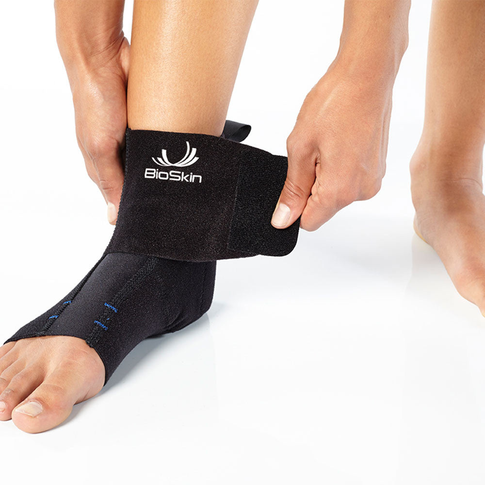 BioSkin black pull-on ankle support sleeve with stabilizing straps wrapped around a foot and ankle — view 4